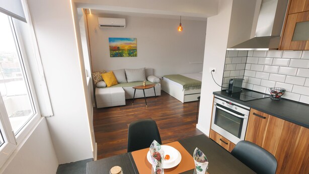 A compact living space with a dining area, kitchenette, and a sofa in the background. - Serdica Tower View DT Parking Wi-Fi AC (Sofia)