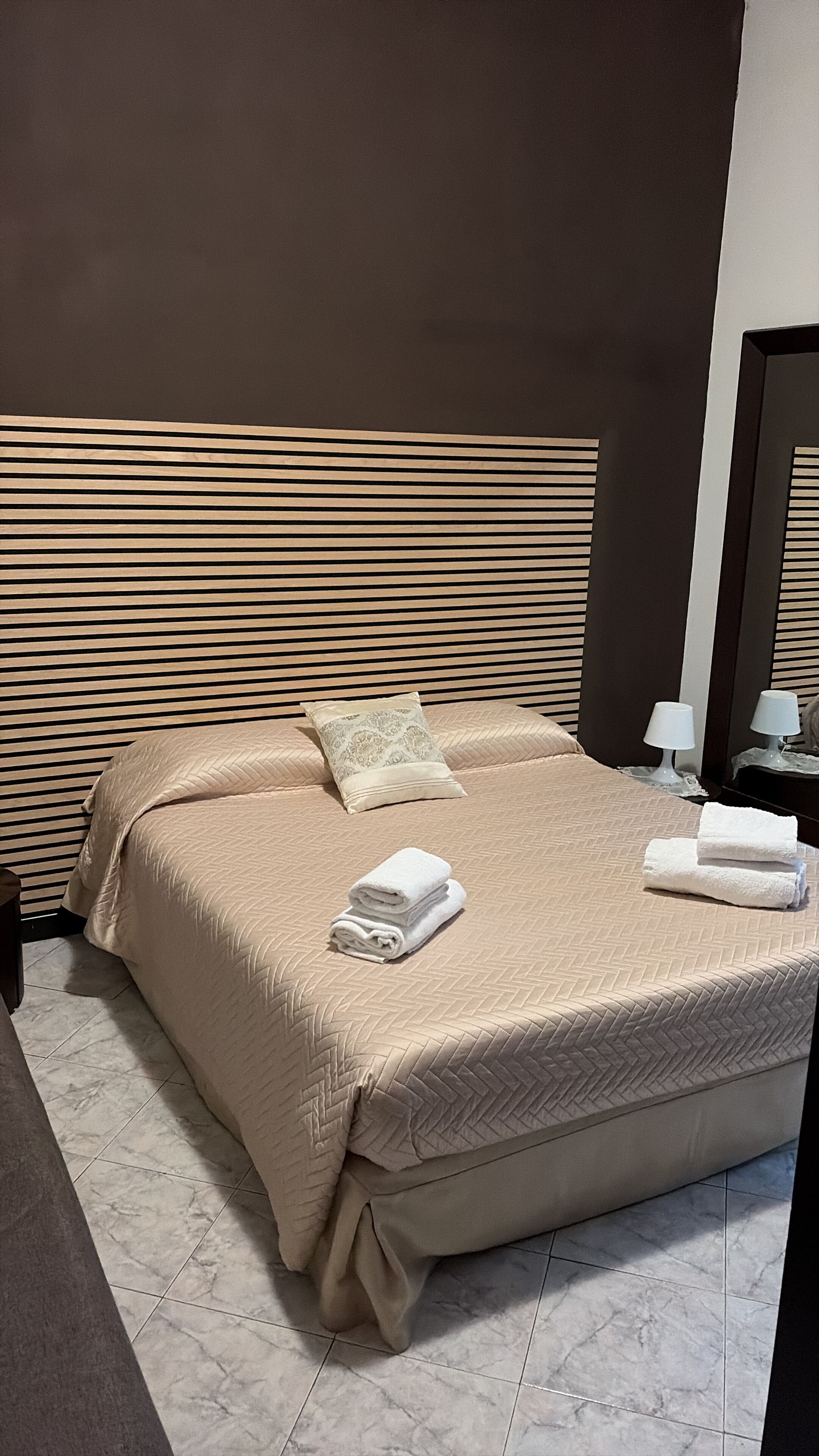 Un lit bien fait, avec une couette beige, deux oreillers et des serviettes pliées.