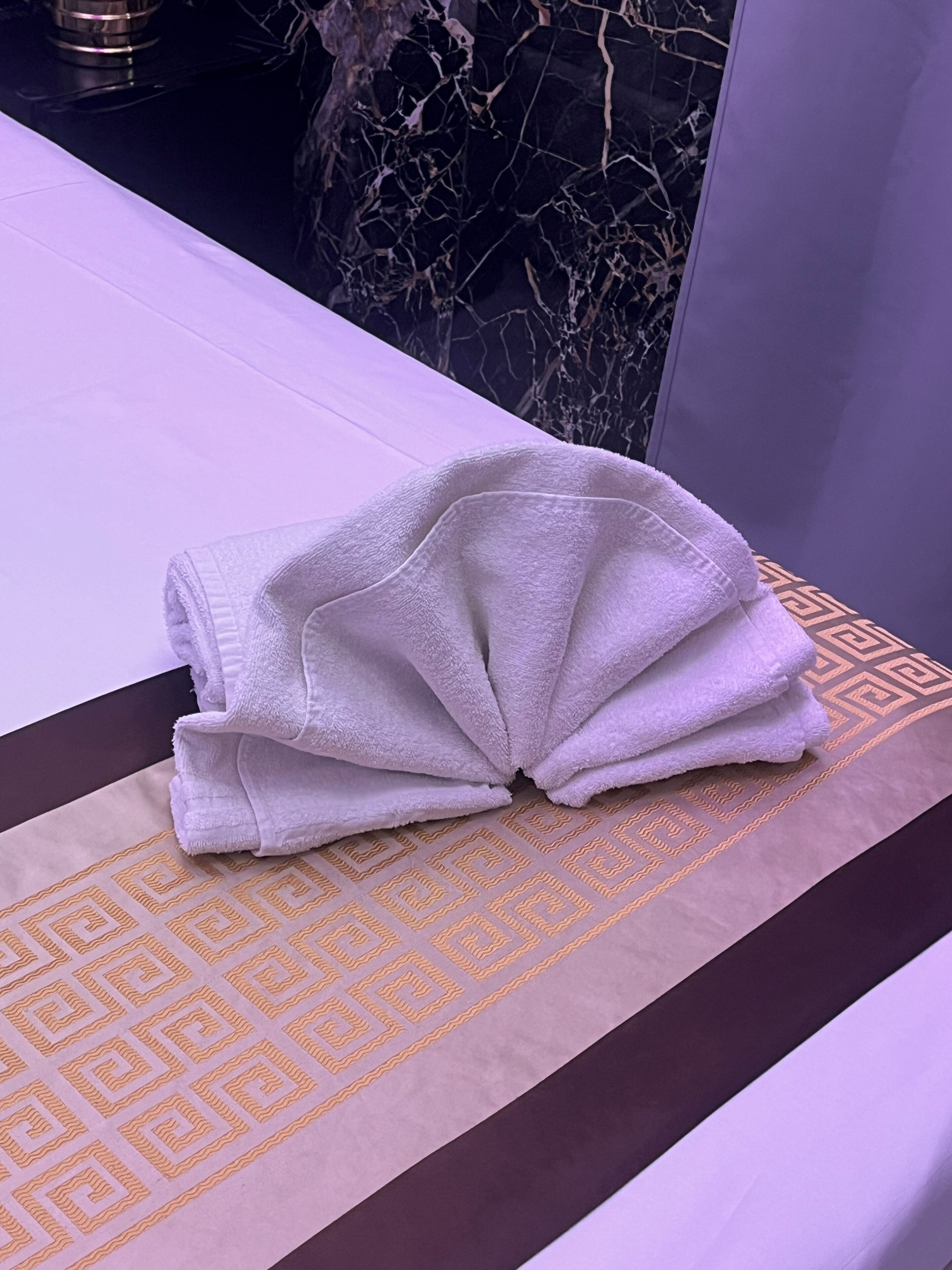 A neatly folded white towel on a patterned bath mat in a bathroom with a marble backsplash.