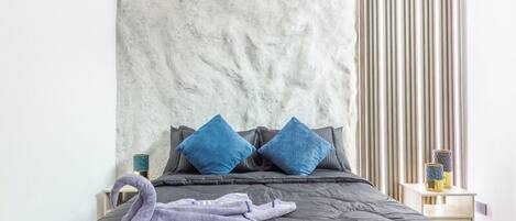 Ein Bett mit einer grauen Bettdecke, zwei blauen Kissen und einem violetten Handtuch.