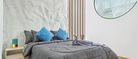 A bedroom with a bed, a nightstand, a window, and a view of buildings.