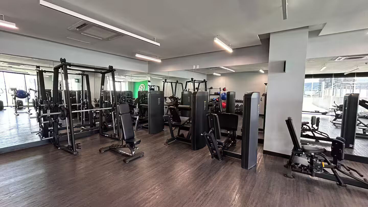 Une salle de sport équipée de divers appareils d’exercice, dotée de grandes fenêtres et présentant un design moderne et épuré.
