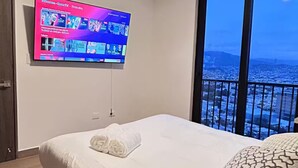 Ein modernes Hotelzimmer mit einem großen Bett, einem flachbildfernseher an der Wand und einem Balkon mit Blick auf die Stadt.