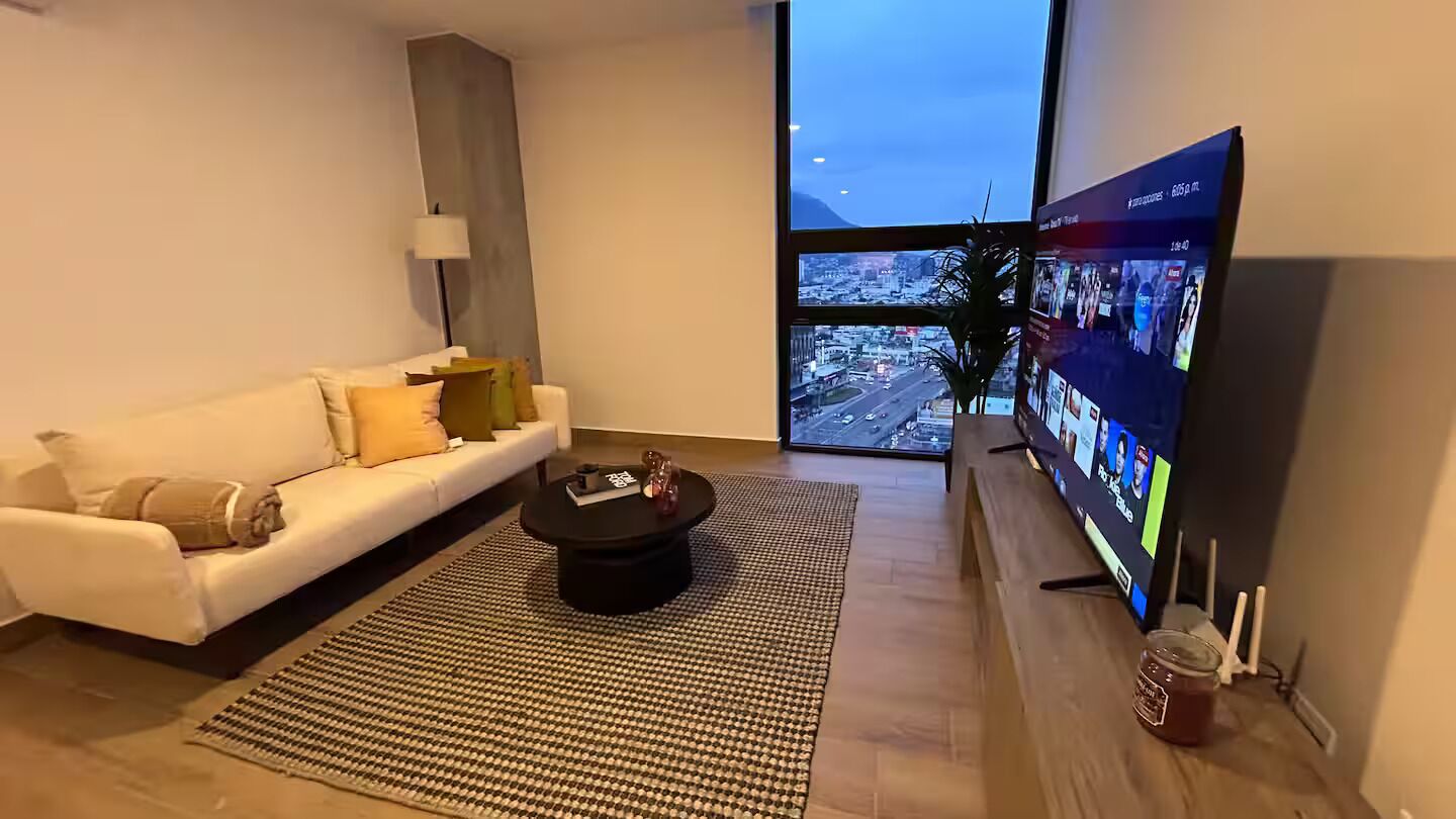 Ett modernt vardagsrum med en soffa, ett soffbord och en stor TV-skärm som visar en vy över en stad.