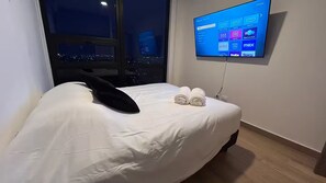 A hotel room with a bed, a window with a view of a cityscape at night, and a mounted TV displaying various streaming services. - Luxury PH, 3 BR w stunning views - 9 guests (Monterrey)