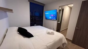 Ein Hotelzimmer mit Bett, einem an der Wand befestigten Fernseher und Blick auf die nächtliche Stadt.