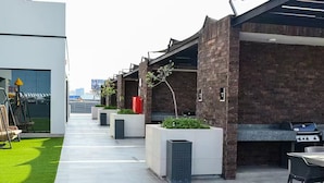 Een modern buitenpatio met een lange opgang, plantenbakken en een barbecuehoek.