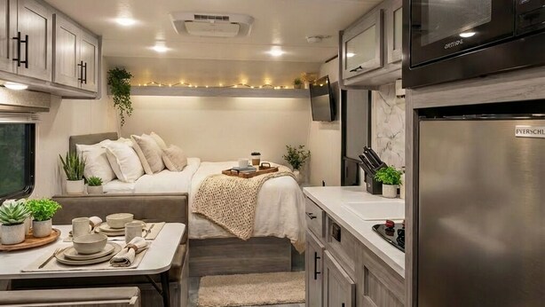 A compact RV kitchen with a bed, kitchenette, and dining area.