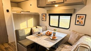 A cozy RV interior with a dining area, seating, and a window with a view.