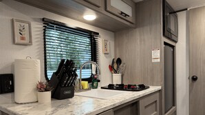 A compact kitchen with a marble countertop, a sink, and a window with blinds.