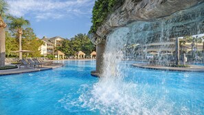 Ein Pool mit Wasserfall, Liegestühlen und einem Gebäude im Hintergrund.