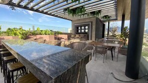 Un'area bar all'aperto con un lungo bancone, varie opzioni di seduta e vista sulla città.