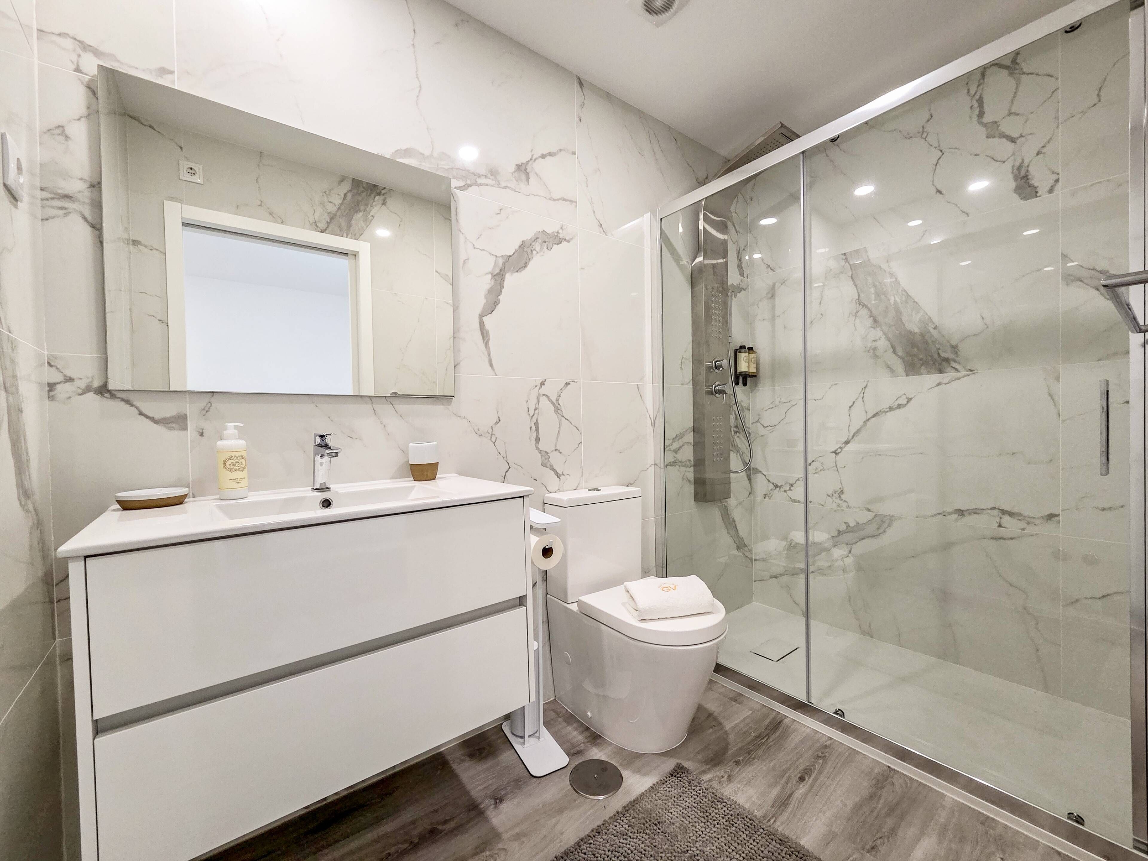 A modern bathroom with a marble backsplash, a glass shower enclosure, and a white vanity with a mirror.