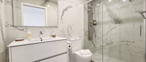 A modern bathroom with a marble backsplash, a glass shower enclosure, and a white vanity with a mirror.