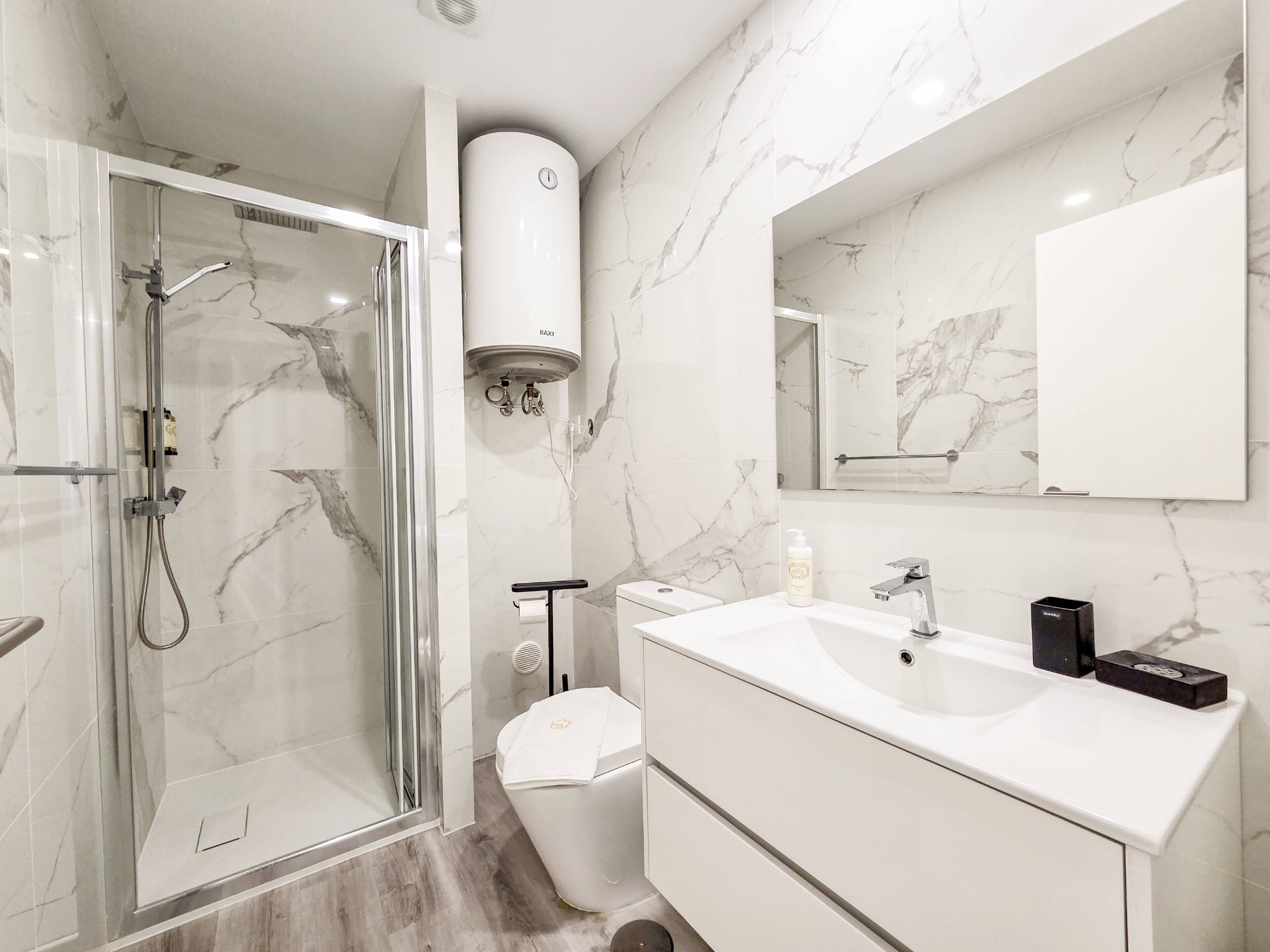 Un baño moderno con ducha envuelta en vidrio, inodoro, lavabo con espejo y toallero.