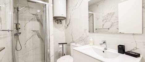 Un baño moderno con ducha envuelta en vidrio, inodoro, lavabo con espejo y toallero.