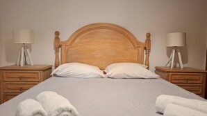 A neatly made bed with white linens, two pillows, and two rolled towels on the side. There are two bedside tables with lamps and a wooden headboard. - PRAIA DA ROCHA - ATLANTICO IV (Portimão)