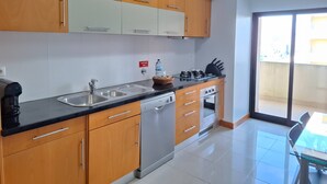 A modern kitchen with wooden cabinets, a gas stove, a dishwasher, and a large window. - PRAIA DA ROCHA- CASA DA PRAIA 904 (Portimão)