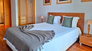 A neatly made bed with a grey throw blanket, wooden headboard, and two bedside lamps. - PRAIA DA ROCHA- CASA DA PRAIA 904 (Portimão)