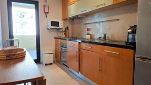A kitchen with wooden cabinets, a microwave, a stove, and a refrigerator. - PRAIA DA ROCHA- CASA DA PRAIA 702 (Portimão)