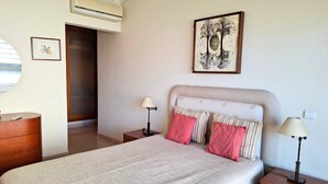 A neatly arranged bedroom with a bed, bedside tables, a lamp, and a framed artwork on the wall. - PRAIA DA ROCHA- CASA DA PRAIA 702 (Portimão)