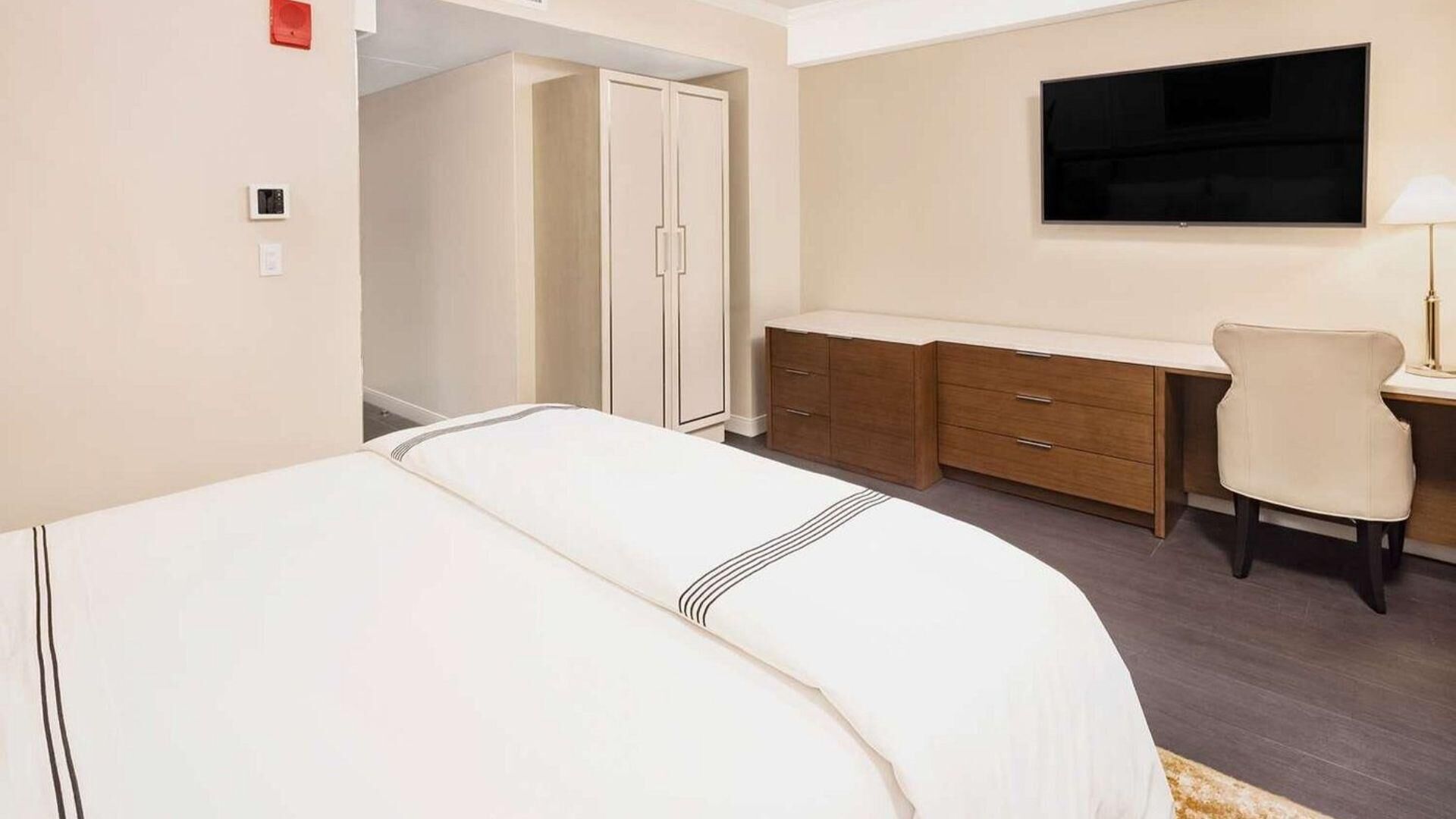 A hotel room with a bed, a desk, a chair, a wardrobe, and a TV.