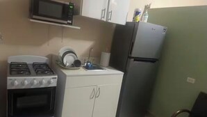 Kompakti keittiö, jossa on kaasuliesi, mikroaaltouuni, jääkaappi ja valkoiset kaapit.