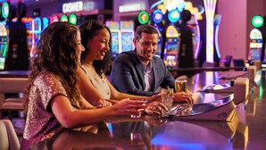 Un groupe de personnes est réuni dans un bar, avec des machines à sous en arrière-plan.