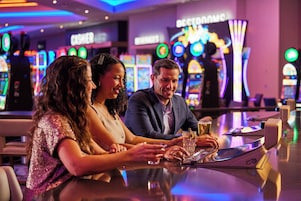 Un grupo de personas en un bar, con máquinas tragamonedas al fondo.