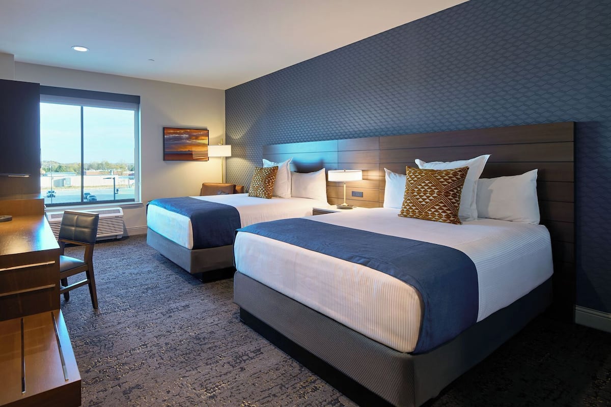 A hotel room with two beds, a desk, and a chair.
