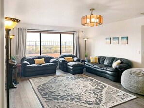 A living room with a large window, two black leather sofas with yellow cushions, a patterned rug, and a hanging light fixture. - Lake Powell 4 BR, hot tub, on golf course, views (Page)