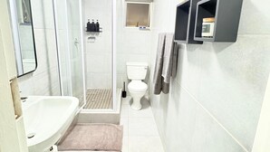 Un bagno con doccia, WC e lavandino. Si vedono scaffali con articoli da toilette e un porta asciugamani.
