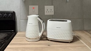 Una cucina con ripiano in legno, una pianta in vaso, tre contenitori bianchi con etichette e un tostapane.
