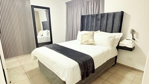 Una camera d'albergo moderna con un letto grande, un comodino con una lampada e uno specchio a parete.
