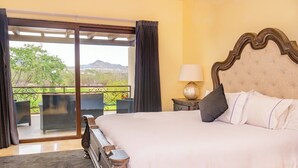 Un dormitorio con una cama grande, una mesita de noche, una lámpara y vistas a un balcón con mobiliario exterior.