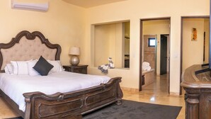Un dormitorio con una cama grande, dos mesitas de noche con lámparas, un espejo y una puerta que da a otra habitación.