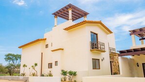 Una casa de dos pisos con balcón, pérgola y un pequeño jardín.