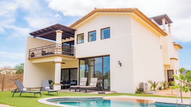 Una casa de dos plantas con balcón, piscina y mobiliario de exterior.