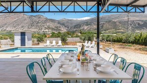 A dining table set for six with chairs, a pool, and mountains in the background. - Casa Rural Las Flores Nigüelas by Ruralidays (Granada)