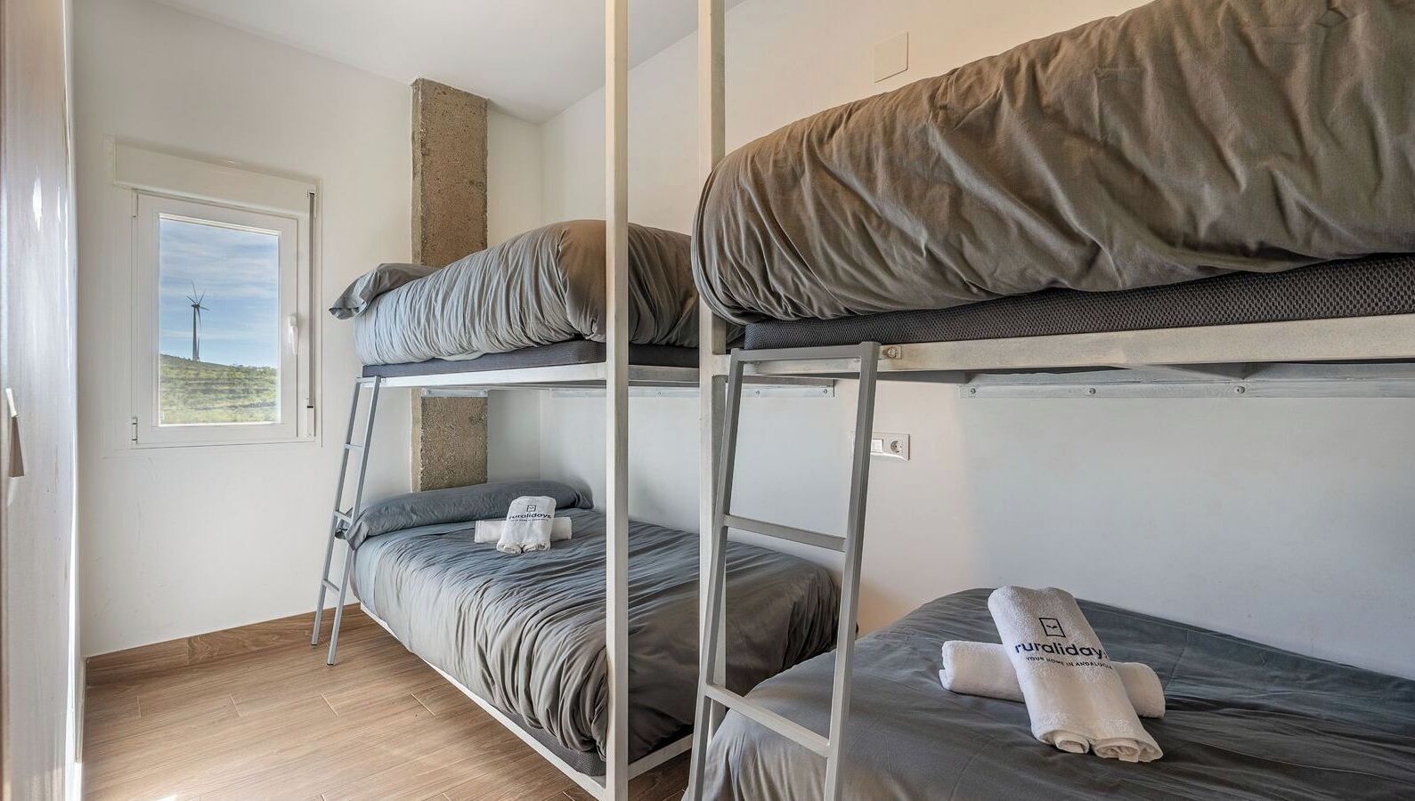 A dormitory-style room with bunk beds, a window with a view of a landscape, and a ladder for accessing the upper bunk.