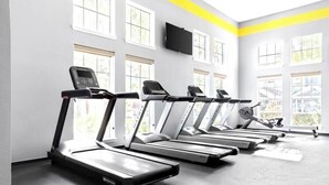 Una palestra con tapis roulant allineati, ampie finestre e un televisore montato a parete.