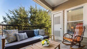 Ein Balkon mit einer Couch, einem Schaukelstuhl und einem kleinen Tisch mit Blumen.