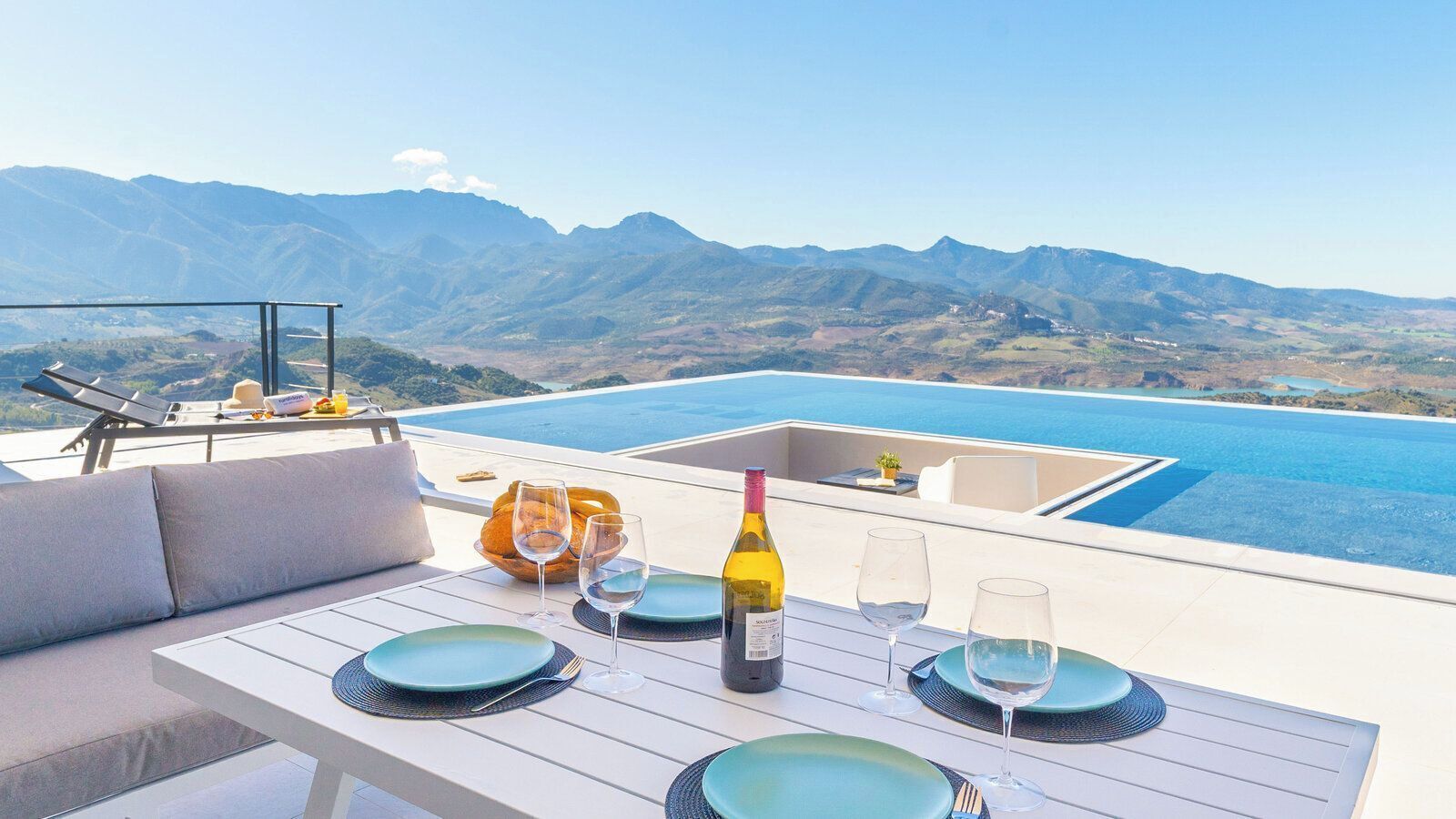 A dining area with a table set for two, overlooking a pool and mountains.