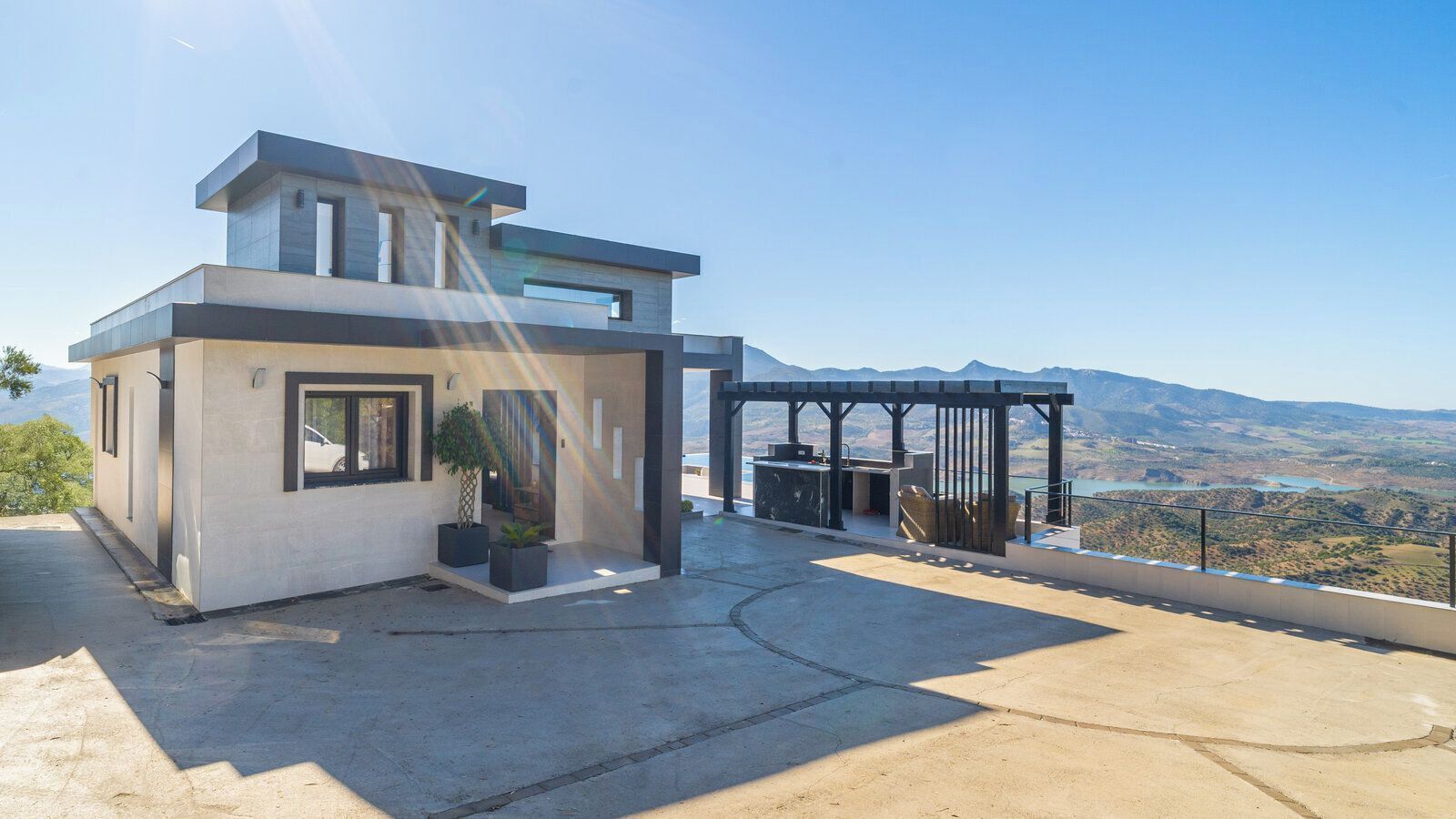 Ein modernes, zweistöckiges Haus mit Terrasse, einer Pergola und Blick auf eine schöne Berglandschaft.