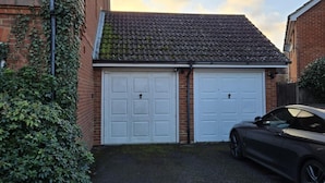 A garage with two white doors, a black car parked inside, and a brick wall with ivy. - Garden - Pets - Parking - Wifi - Sleeps 2 (Ashford)
