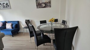 A modern living room with a blue sofa, a glass dining table with black chairs, and a vase with sunflowers. - Garden - Pets - Parking - Wifi - Sleeps 2 (Ashford)