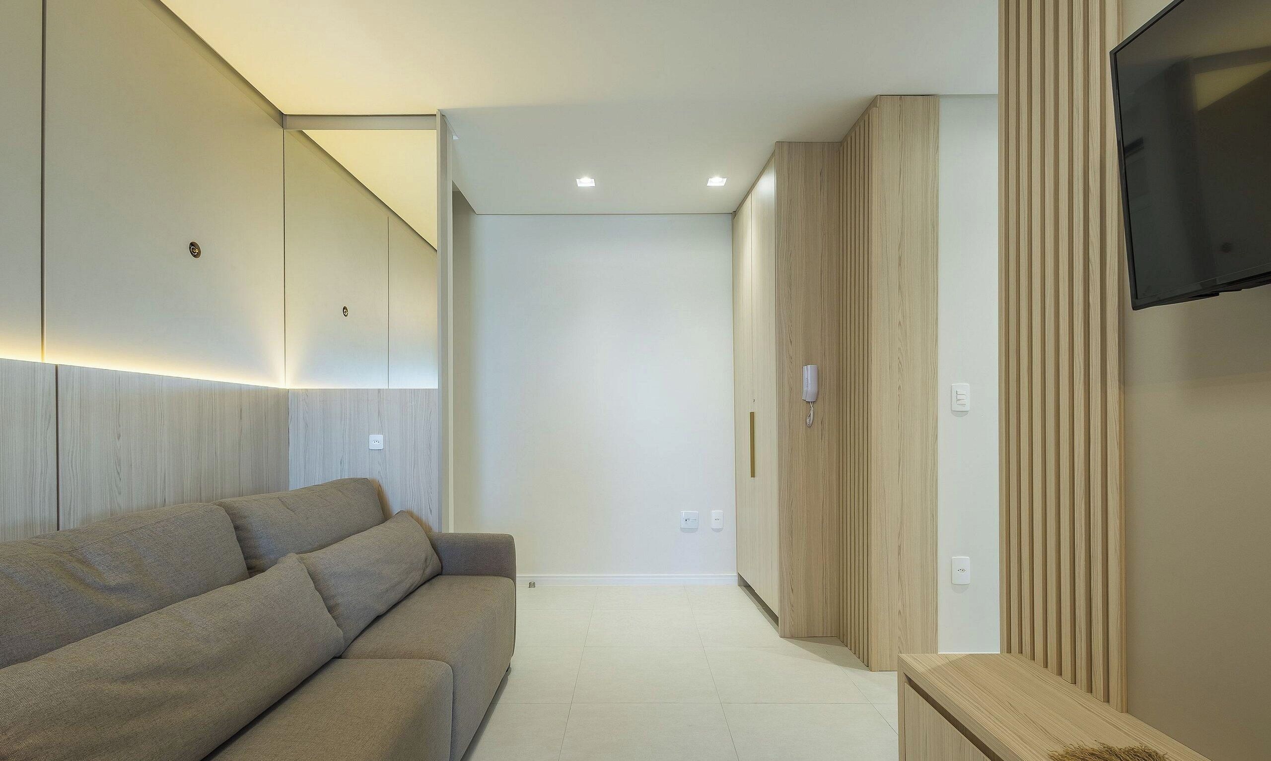 A modern living room with a sofa, a television mounted on the wall, and a wooden wardrobe.