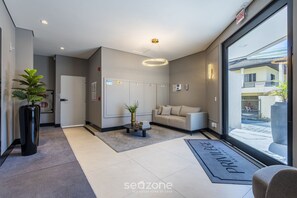 Eine moderne Hotellobby mit einer Rezeption, einer Sitzecke, einem Topf mit einer Pflanze und einem großen Fenster mit Blick nach außen.