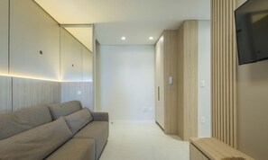 Ein modernes Hotelzimmer mit einer Couch, einem an der Wand montierten Fernseher und einem Holzschrank.