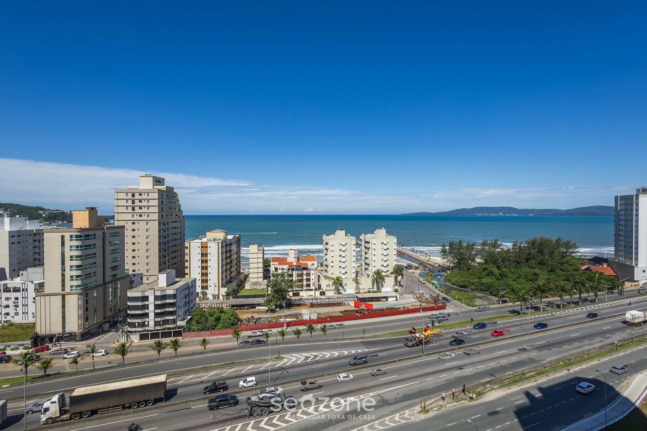 A coastal cityscape with modern buildings, a busy road, and a clear view of the ocean.